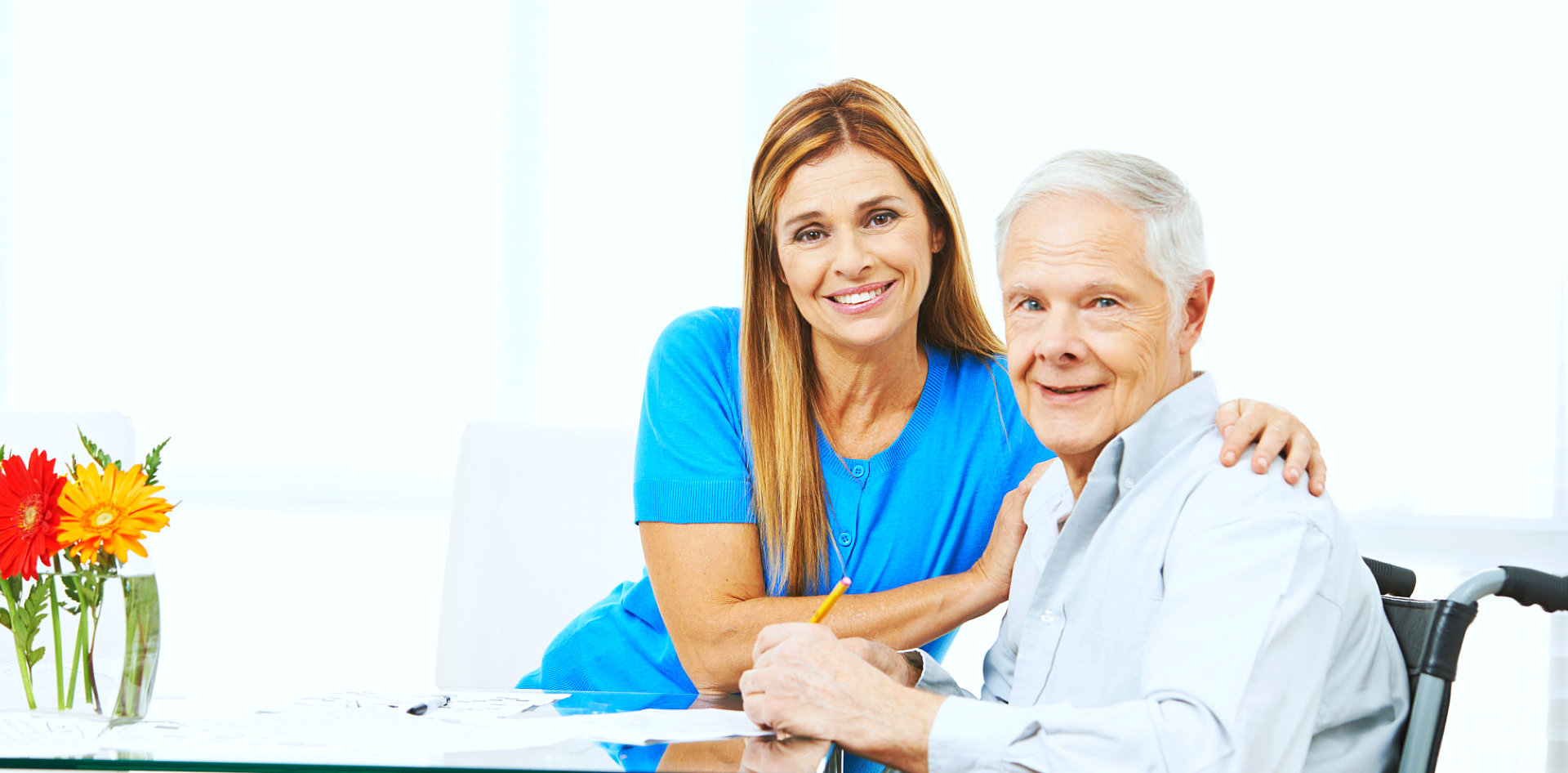 caregiver and senior man are smiling while he is writing at the paper